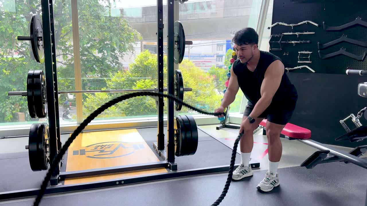 Athletic man vigorously trains with battle ropes in bright, spacious gym with natural daylight