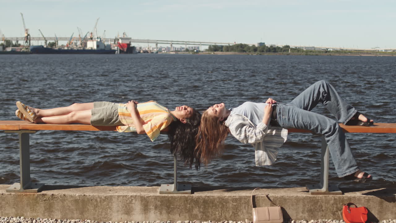 Female Best Friend Lying on Bench at Waterfront