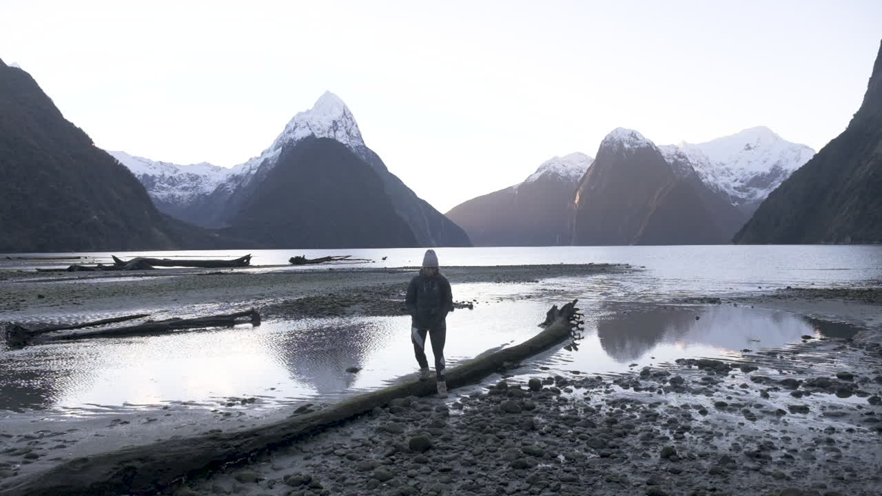 Slowmotion-optagelse af pige i vandreudstyr med kamera, der går langs Milford Sounds kystlinje