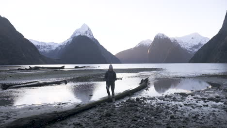 slow motion shot of girl in hiking gear with camera walking along milford sound shoreline