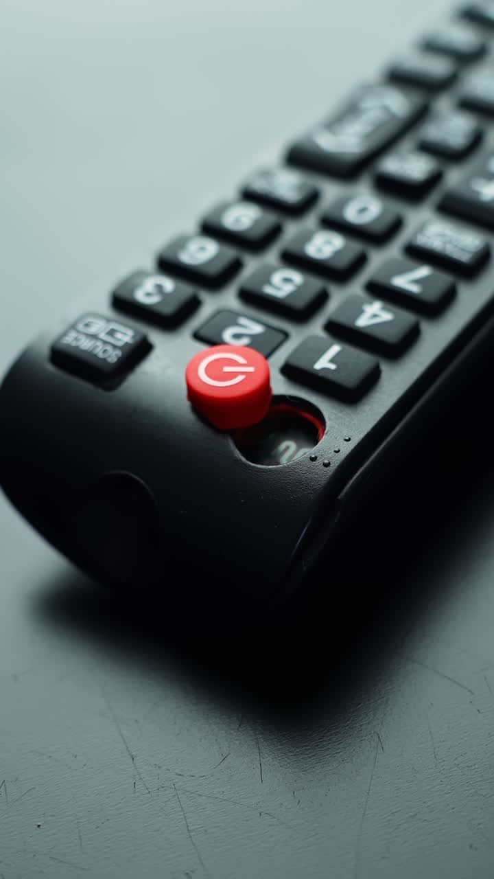 Scatto macro verticale di un telecomando TV nero con pulsante di accensione rosso a fuoco nitido, profondità di campo ridotta e sfondo sfocato, con spazio per il testo per concetti di interfaccia utente tecnologica.
