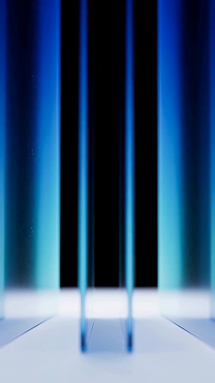 Video verticale: Luce cangiante che avvolge tre pannelli blu traslucidi su un set, rivelando un vuoto centrale.