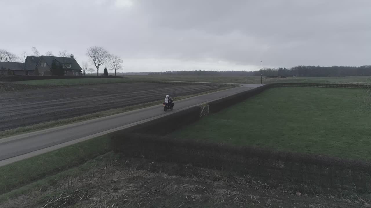 Drone following close on motorcyclist driving between farm roads