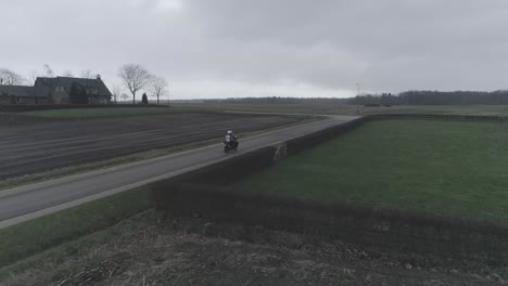 drone following close on motorcyclist driving between farm roads