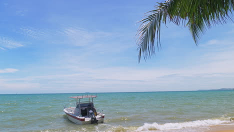 A-boat-with-an-outboard-motor-moored-very-close-to-the-beach-moving-with-the-waves-in-Pattaya,-Thailand,-world-famous-for-its-beaches-and-resorts