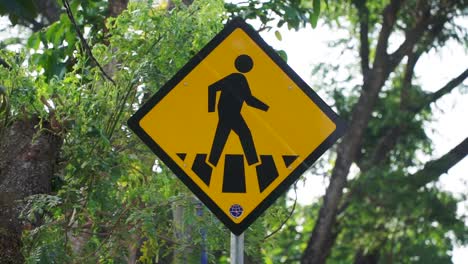 pedestrian crossing sign with lush green tree leaves on the background