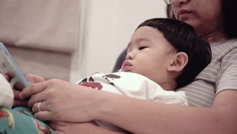 asian baby using mobile phones with mom on the bed