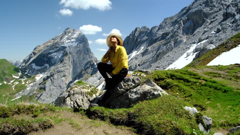a woman resting on a rocky stone, enjoying a sunny day with the mountain rocks in the background