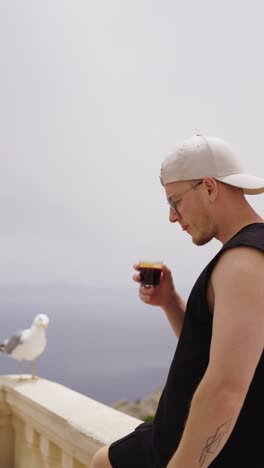 vertical shot of male tourist sip black coffee with seagull on balcony, spain