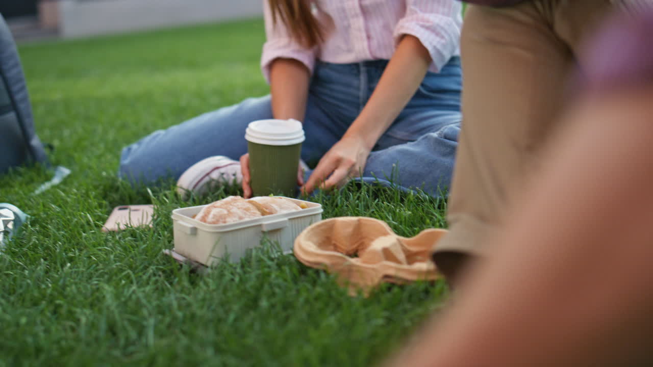 편안한 소녀 얘기 피크닉 앉아 녹색 풀. 클로즈업 손 커피 컵을 들고