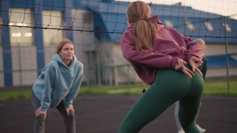 back view of lady slightly bent making gestures, with two other ladies blurred in background in similar posture during outdoor physical training activity, engaging in teamwork