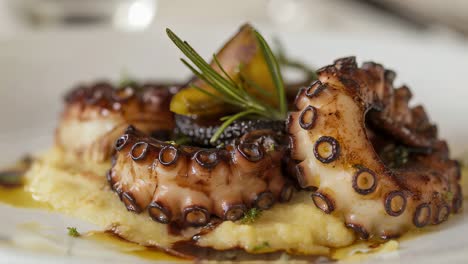 octopus tentacle seasoned with rosemary and olive oil lies on a bed of mashed potatoes and is decorated with a sprig of rosemary and a balsamic vinegar reduction