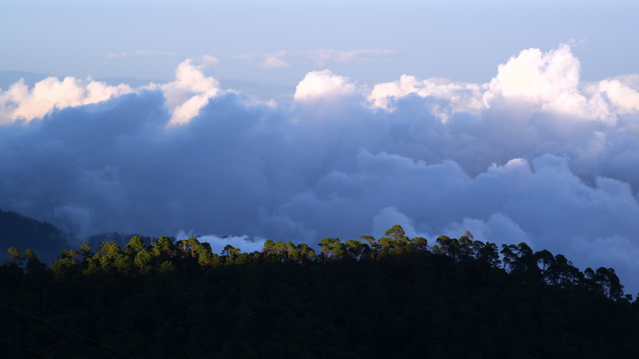 Wide shot of clouds moving rapidly over a forested mountain. The dynamic sky and lush trees create a dramatic and cinematic natural landscape, perfect for outdoor and travel scenes