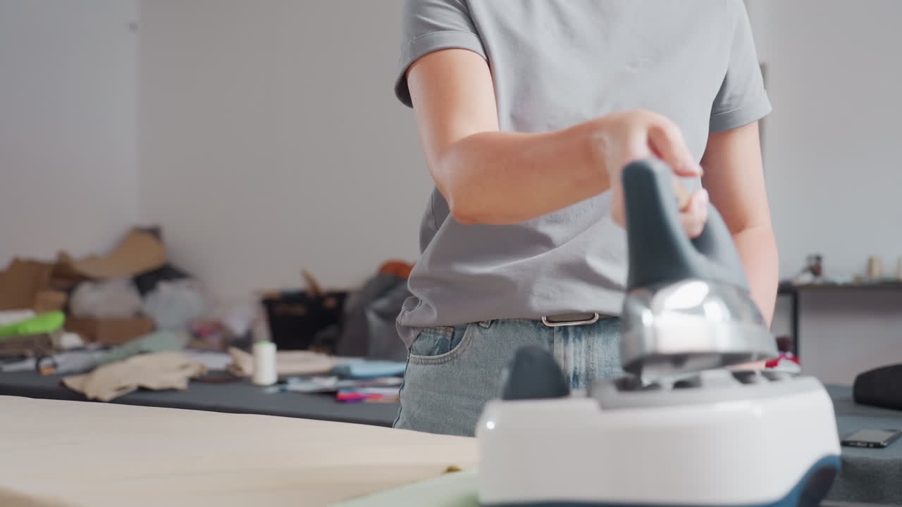 Two women in fashion studio, one ironing while other arranges colorful fabrics, focusing on garment production, demonstrating professional technique, creativity shining in collaborative environment