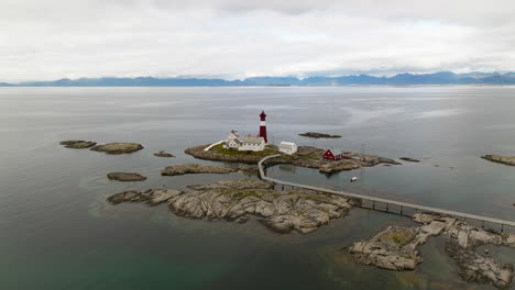 Red-lighthouse-with-white-band-stands-alone-on-exposed-rocky-island,-aerial-establish