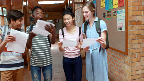 happy classmates looking at grade cards in corridor