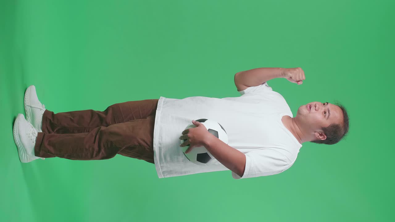 cuerpo lleno de emocionado hombre asiático con una pelota está apoyando para disparar a la meta mientras aplaude el fútbol en el fondo de la pantalla verde