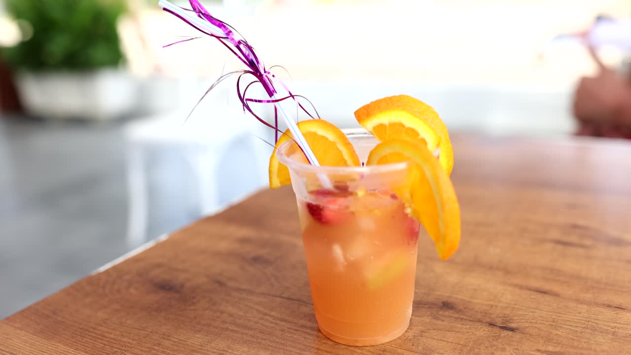 Cocktail all'arancia con cannuccia, fetta d'arancia e fragole sulla spiaggia di mare.