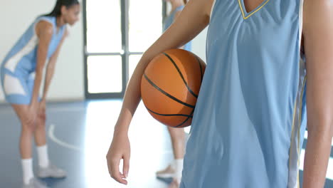 holding basketball, female player standing on court with teammates in background
