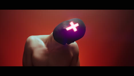 masked man with cross of light glowing on his face moves slowly