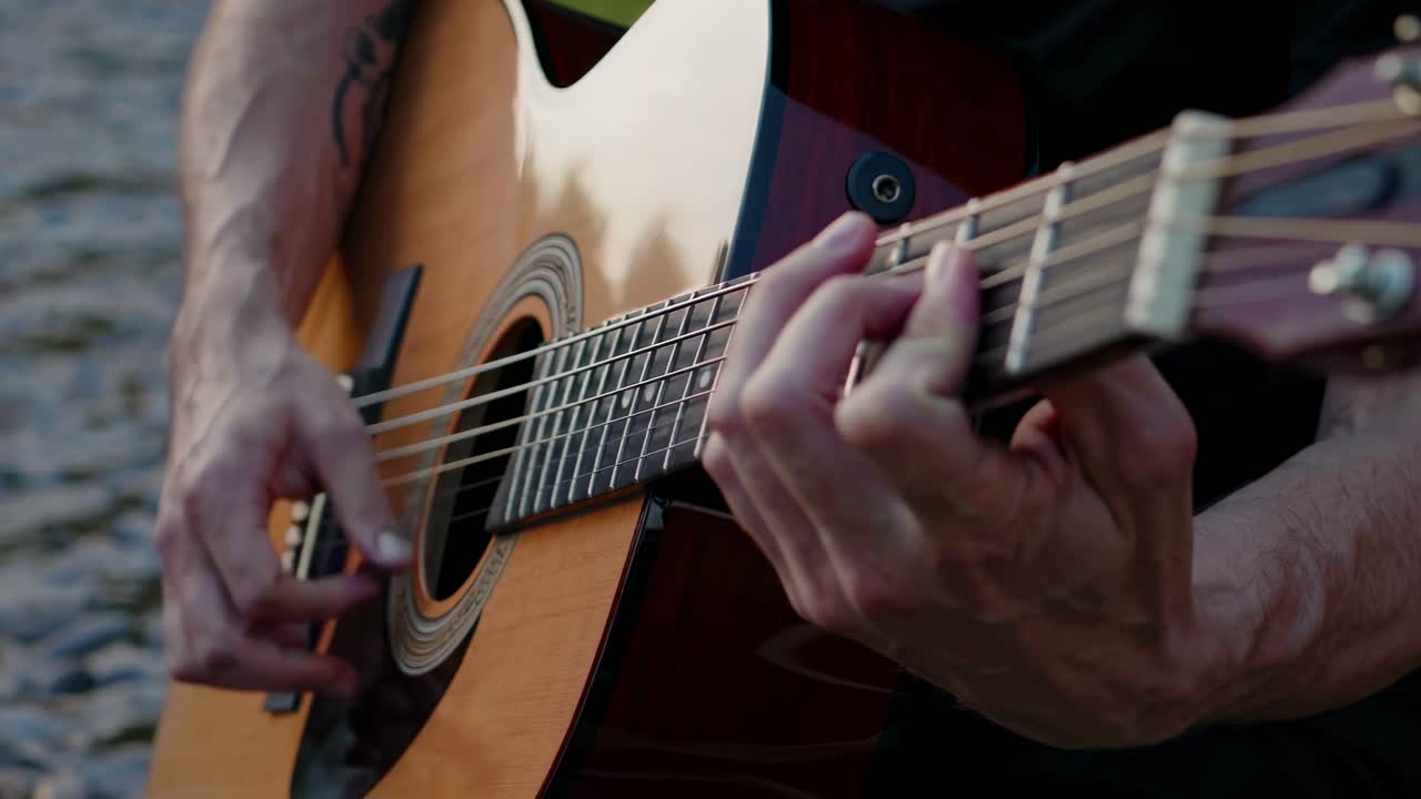Primo piano video di mani che suonano una chitarra acustica in riva all'acqua, che cattura la complessa diteggiatura