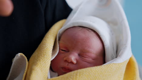 adorable face of a few minutes old baby. little newborn covered in blankets in dad's hands. close up.