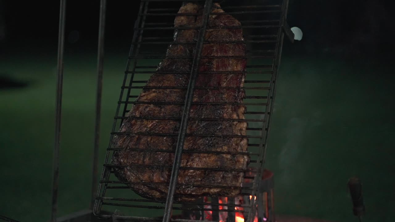 Großes Stück argentinischer Barbecue-Rippchen gart auf einem Außengrill bei einer Abendveranstaltung.