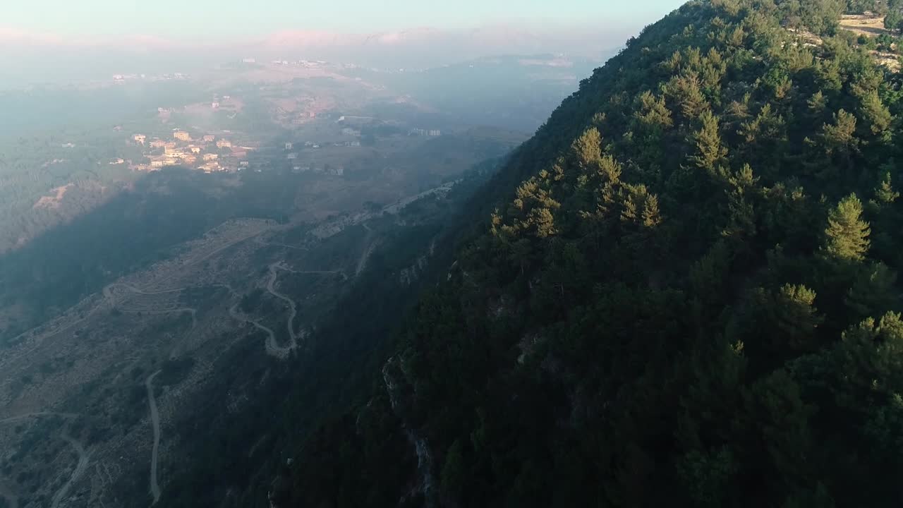 Aerial flight toward pine trees over cliff tilt down to high elevation panoramic view