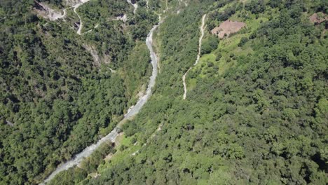 Drone-shot-revealing-a-river-stream-and-narrow-road-through-a-mountain-landscape-with-the-view-of-the-city-of-Zacatlan-in-the-background,-Puebla,-Mexico