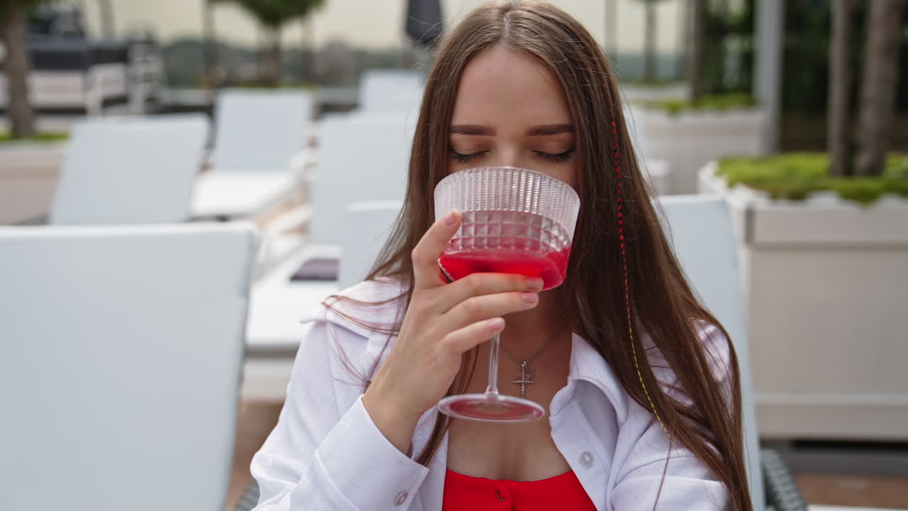 Attractive long-haired lady drinking red cocktail sitting in deckchair. Girl having vacation at the resort in summer. Close up.