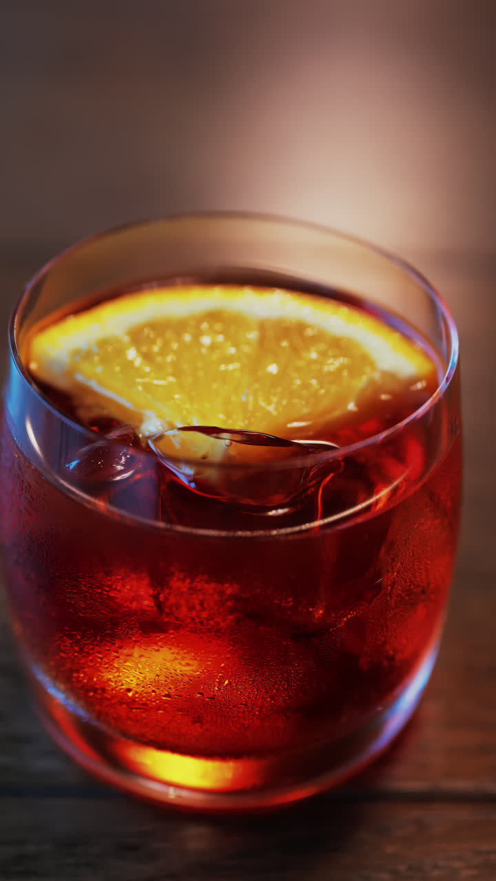 Close up of a Negroni cocktail with orange slice and ice cubes on a wooden table