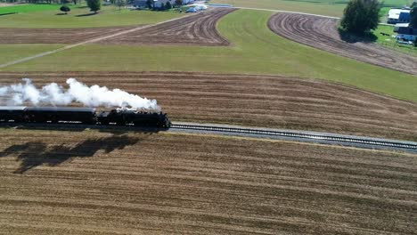 steam passenger train puffing smoke along amish countryside as seen by a drone