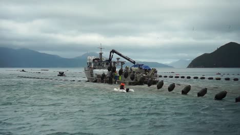 Man-on-small-inflatable-boat-approaching-mussel-boat-at-plantation-on-cloudy-day