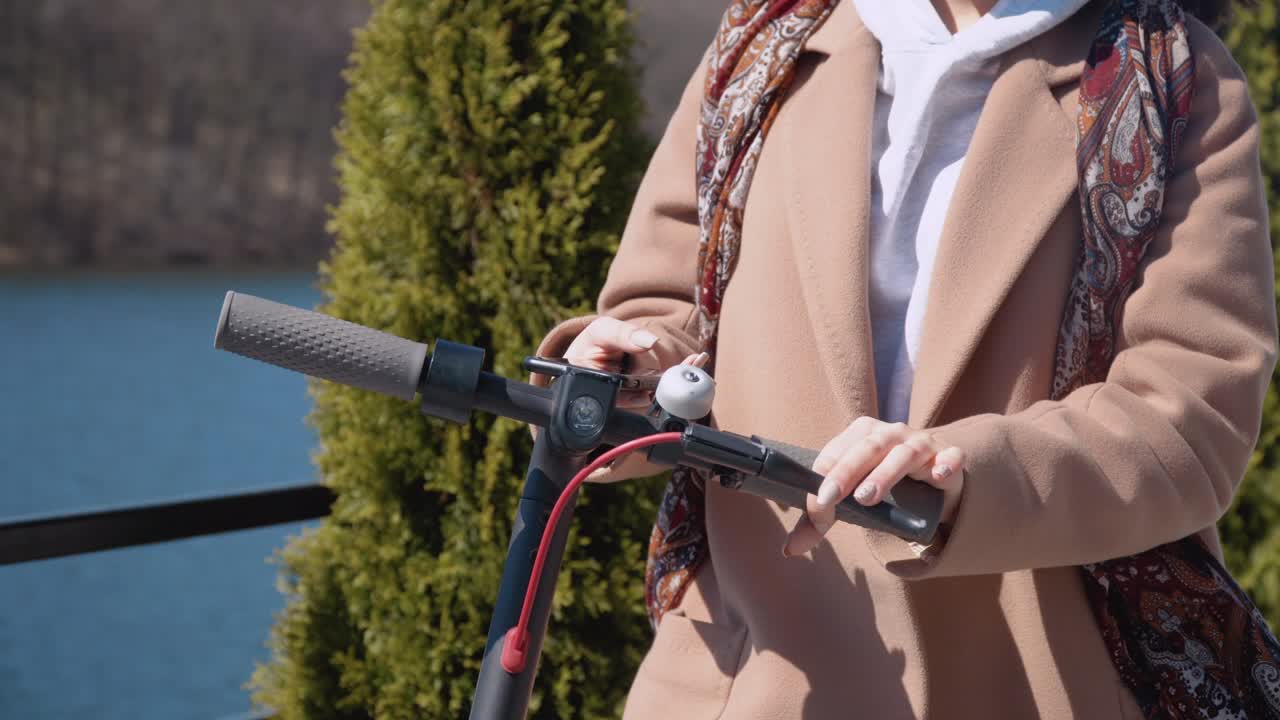 молодая студентка в полусезонной одежде в тусклых цветах берет электрический скутер в совместной парковке. туристическое телефонное приложение