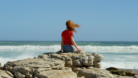 woman sitting on a rock and looking at the ocean waves 4k