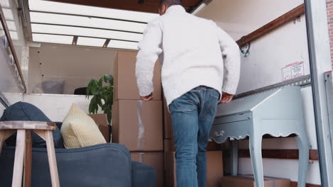 Man-Unloading-Boxes-From-Removal-Truck-Outside-New-Home-On-Moving-Day