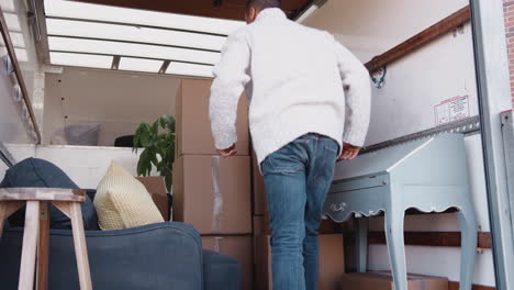 Man Unloading Boxes From Removal Truck Outside New Home On Moving Day