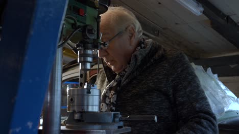 senior metal worker operating drilling machine in a small dark workshop