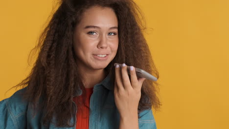 Caucasian-curly-haired-woman-recording-voice-message-on-smartphone.