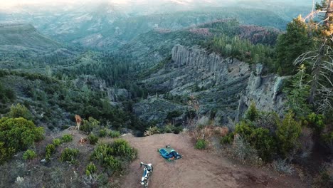 Vista-Aérea-De-Motocicletas-Y-Equipos-De-Camping-En-La-Montaña-Con-Vistas-Panorámicas-Al-Amanecer