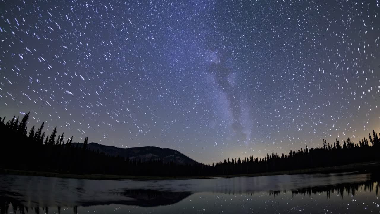 A mesmerizing time-lapse video captures star trails over a serene lake, shot from a low angle