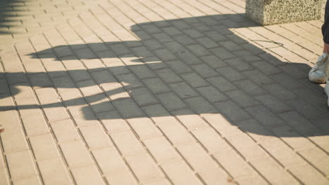 leg view of someone wearing grey joggers and white canvas shoes seated, shadow cast on interlocked floor, the shadow of the individual reflect what the individual is doing