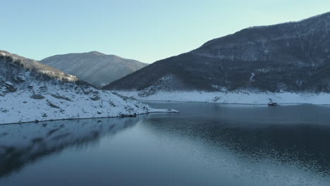 Antena:-Volando-Sobre-Un-Lago-De-Montaña-En-Sus-Orillas-Tiene-Colinas-Cubiertas-De-Nieve,-Que-Se-Reflejan-En-Las-Aguas-Del-Lago