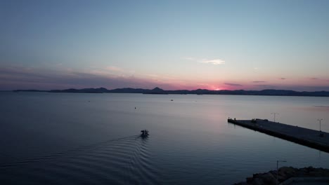 El-Brillo-Rojo-De-La-Hora-Azul-Del-Anochecer-Tiñe-El-Cielo-Mientras-Un-Barco-Solitario-Sale-Del-Puerto,-Con-Una-Estela-Detrás