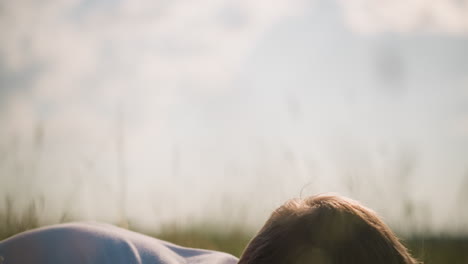 a young boy wearing glasses and a white shirt is lying on the grass in a sunny field. his relaxed expression captures a peaceful and contemplative moment, enjoying the tranquility of nature