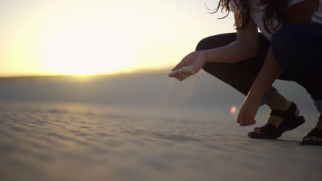 young female traveller gran handful of sand standing in sandal over dry desert during sunset, explore remote nature mother earth