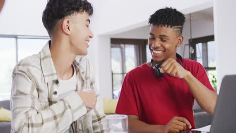 three happy diverse male teenage friends using laptop and talking at home, slow motion