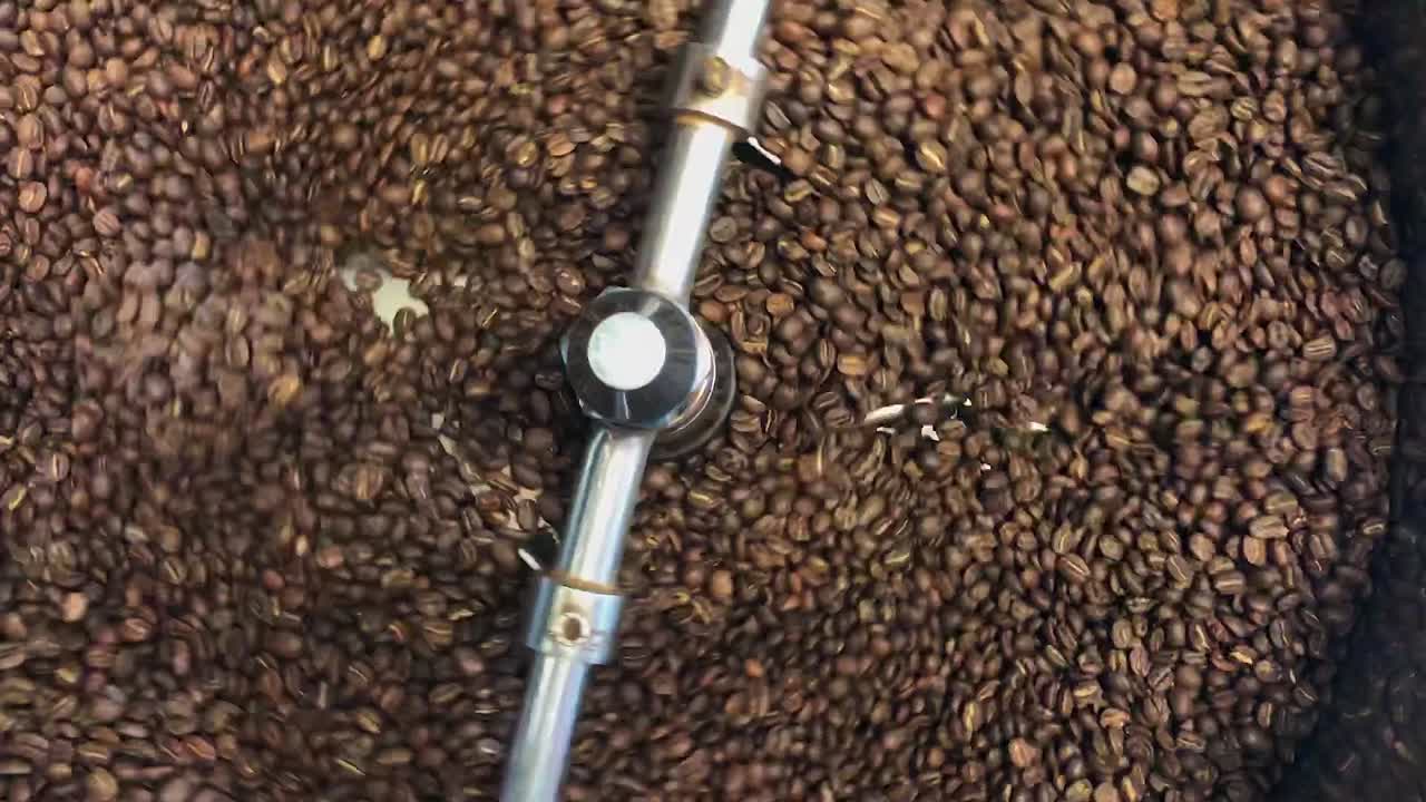 Vista dall'alto: Chicchi di caffè marrone intenso mescolati in una tostatrice in acciaio inossidabile
