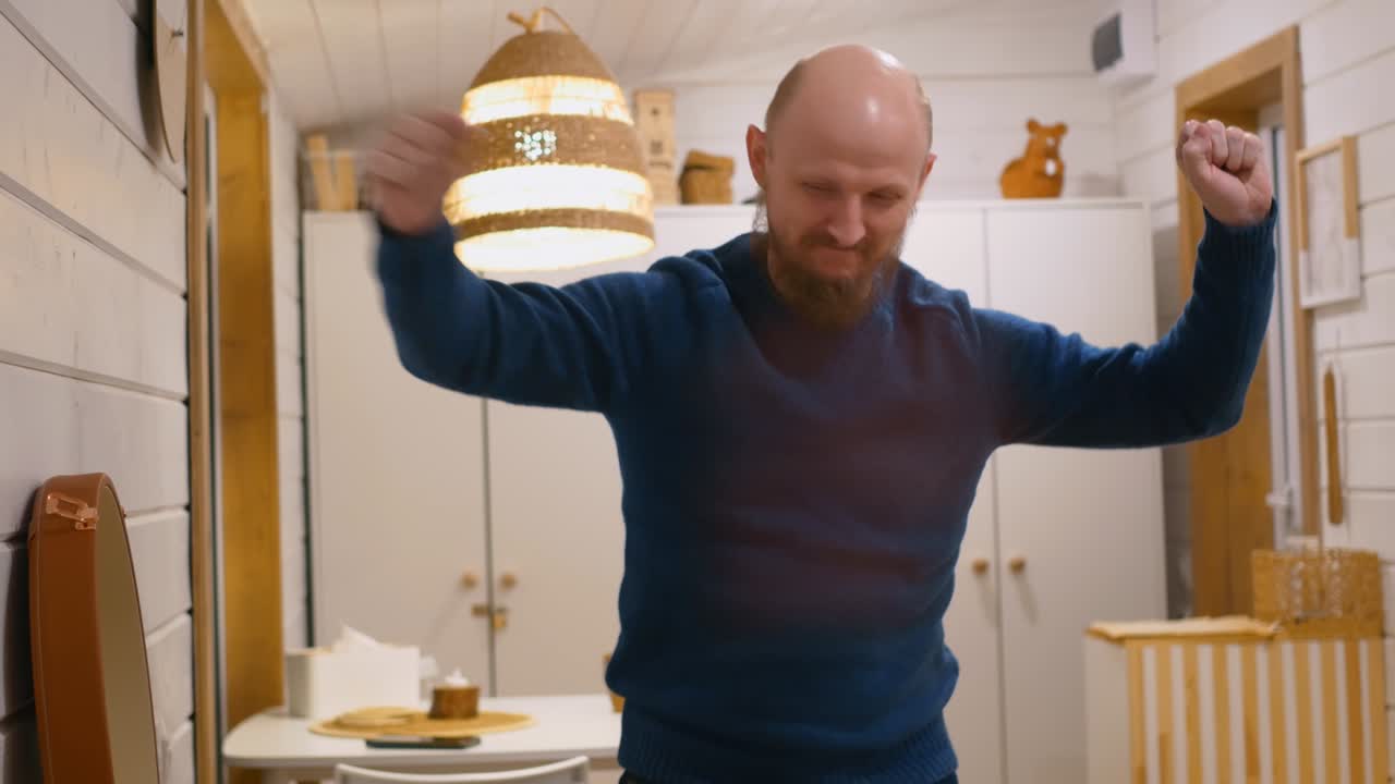 A middle-aged man with a beard dances funny at home while listening to the music of a gramophone with a record. Funny man having fun at the party alone. A bald man is dancing and having fun