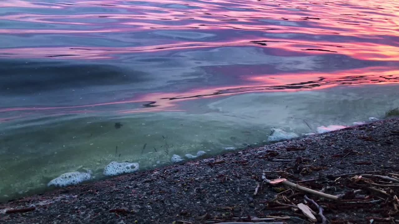 Nærbillede af vandbølger med snavs fra Lerumsøen Aspen i Sverige sent om aftenen ved solnedgang, der skaber flotte farver.